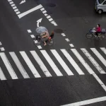 Pedestrians and cyclists crossing a busy city street in rainy weather