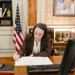 Attorney signing legal documents at desk with scales of justice in a law office